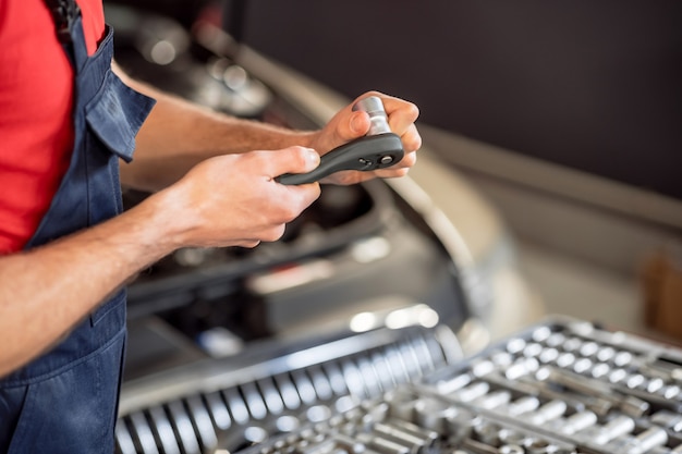 Experiencia, habilidad. Primer plano de manos masculinas que trabajan con parte en el taller de automóviles, la cara de los mecánicos no es visible