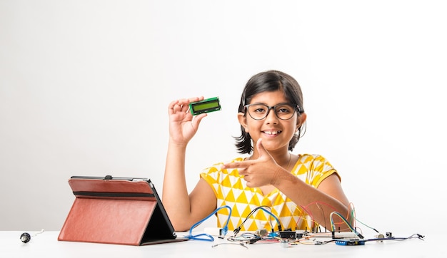 Experimento electrónico: pequeña estudiante india asiática que realiza o estudia ciencias con cables, conexiones, estudia desde una computadora portátil o tableta