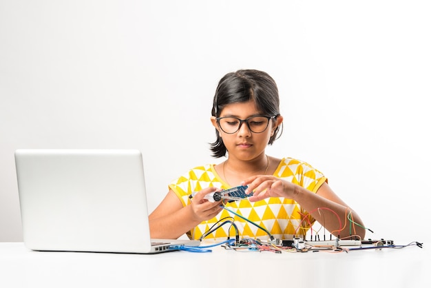 Experimento eletrônico - Aluna asiática indiana pequena fazendo ou estudando ciências com fios, conexões, estudando em um laptop ou tablet