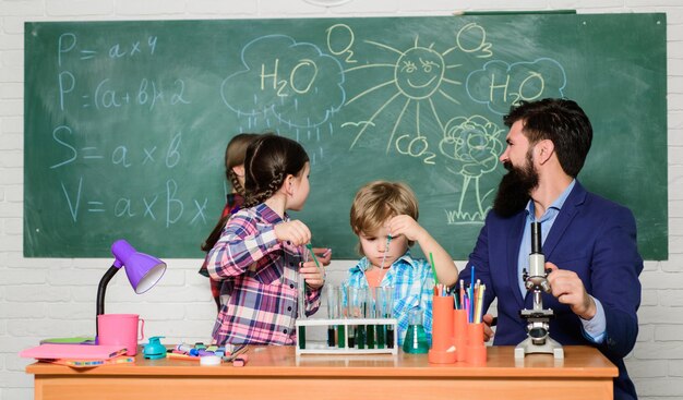 Foto experimento escolar de química fascinante lección de química hombre barbudo maestro y alumnos con tubos de ensayo en el aula explicando química a los niños la ciencia es siempre la solución observe la reacción