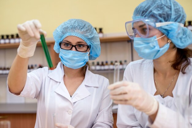 Experimento químico Dos mujeres en uniforme protector con tubos de ensayo en laboratorio