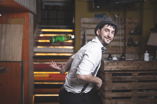 Experto barman con sombrero y pajarita lanzando una botella al aire