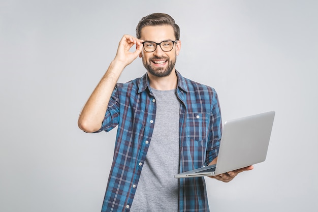 Experto en negocios seguros. Hombre guapo joven confidente en camisa con laptop y sonriendo mientras está de pie contra la pared gris