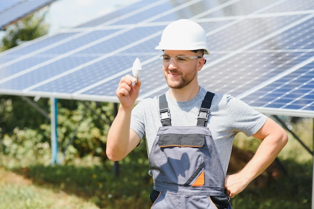 Experto técnico en control remoto de paneles solares fotovoltaicos realiza acciones rutinarias para monitorear el sistema usando energía renovable limpia en la mano una bombilla
