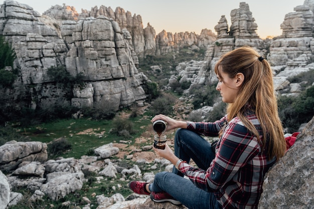 Explorador da jovem mulher que faz o café em um copo na montanha. Conceito de aventura, excursões e viagens.