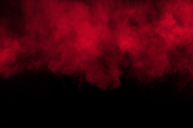 Explosão do pó da cor vermelha no fundo preto. Espirro vermelho das partículas de poeira.