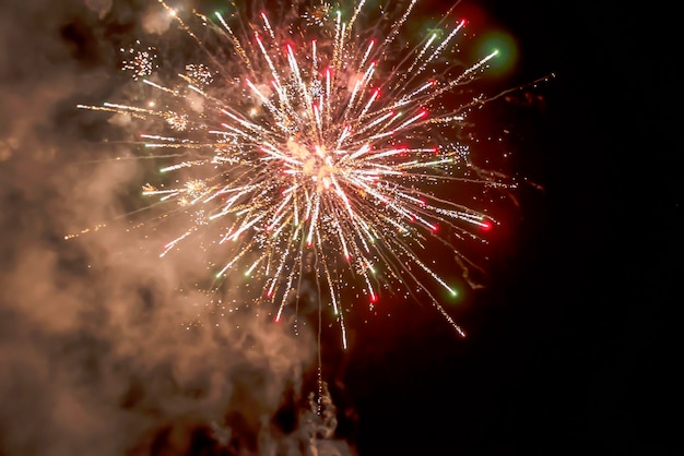 Explosión de fuegos artificiales de hermosas estrellas salpica chispas y líneas brillantes de luces con humo de color rojo y amarillo contra el cielo negro