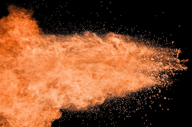 Foto explosión de polvo de color naranja sobre fondo negro.
