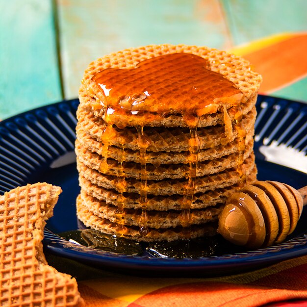 Exposição de waffles caseiros frescos com mel, caramelo, na mesa de madeira verde.