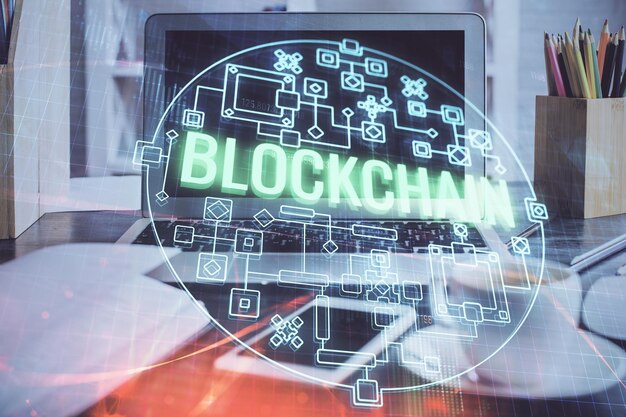 Exposición múltiple del holograma temático de blockchain y criptoeconomía y mesa con fondo de computadora Concepto de criptomoneda bitcoin