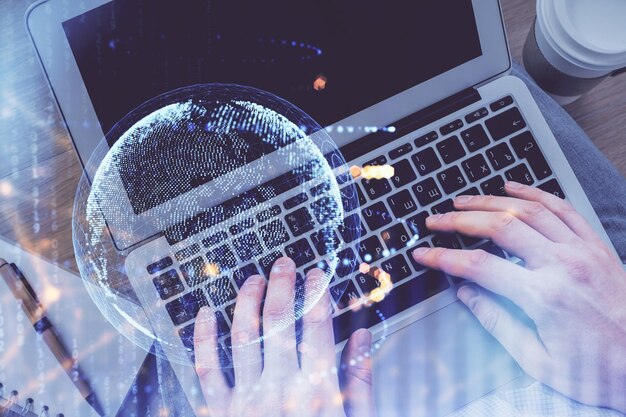 Exposición múltiple de las manos del hombre escribiendo sobre el teclado de la computadora y el holograma del mapa mundial dibujando el concepto de tecnología de vista superior