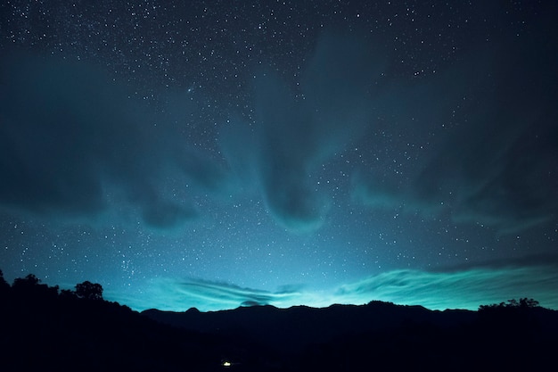 Exposición prolongada y disparo ISO alto de estrellas y nubes sobre la montaña por la noche. efecto de tono azul yo