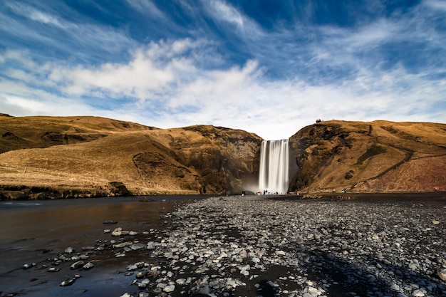 Foto exposición prolongada de skogafoss con agua suave y nubes en movimiento bajo un cielo azul