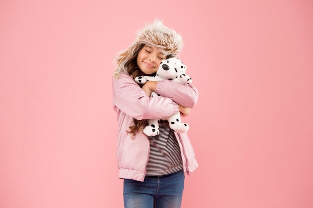 Expresando amor niño feliz fondo rosa temporada fría en ropa de abrigo accesorio niña dálmata perro juguete estilo otoño Infancia felicidad niño moda Hipster niña piel invierno orejera sombrero