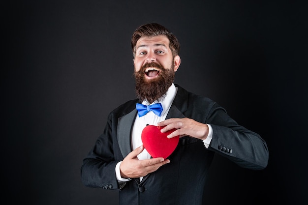 Expresando sentimientos 14 de febrero hombre guapo haciendo propuesta regalo de amor hombre de esmoquin con corazón feliz día de san valentín sé mi amor de san valentín y romance brutal chico barbudo mantenga corazón romántico