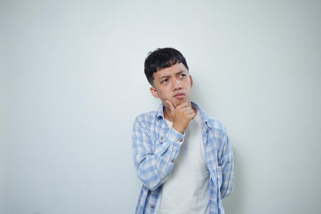 Expresión facial del hombre asiático pensando mientras sostiene la barbilla aislada en el fondo blanco