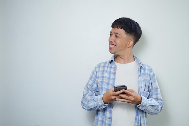 Expresión facial de hombre asiático sonriente mirando de lado mientras sostiene el teléfono móvil