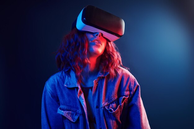Expresión facial de niña con gafas de realidad virtual en la cabeza en neón rojo y azul en estudio