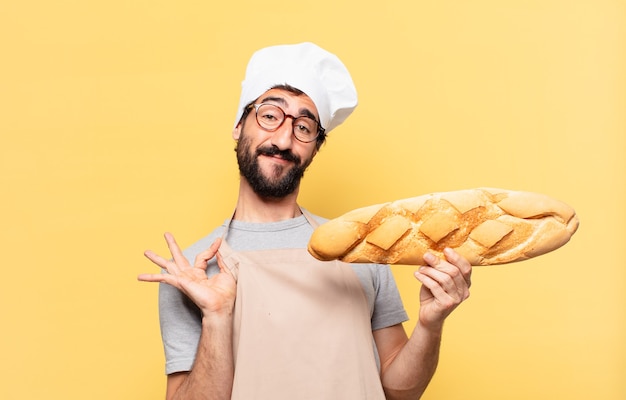 Expresión feliz del hombre joven del cocinero barbudo que sostiene un pan