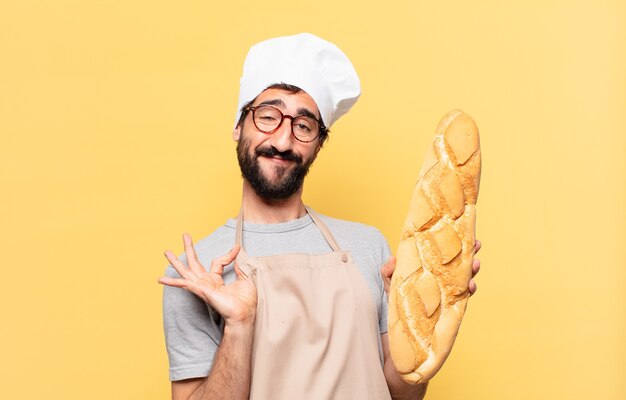 Expresión feliz del hombre joven del cocinero barbudo que sostiene un pan