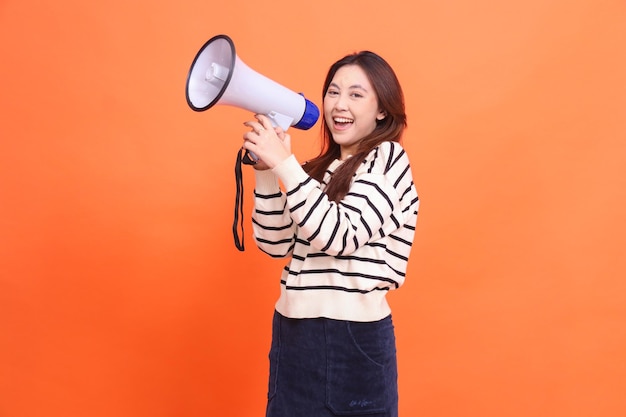 Expresión de mujer asiática gritando felizmente a la cámara de pie con dos manos sosteniendo un megáfono lo