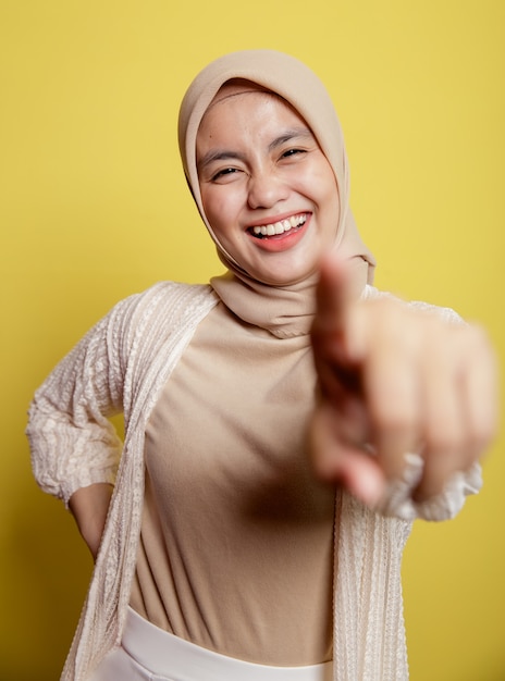 La expresión sonriente de una hermosa mujer con hiyab apunta a la cámara aislada sobre un fondo amarillo