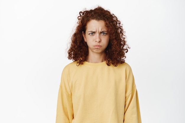 Expresiones faciales y concepto de personas. Joven malhumorada mujer rizada haciendo pucheros, malhumorada y frunciendo el ceño molesta, luciendo ofendida, sin ganas de hablar, de pie sobre fondo blanco