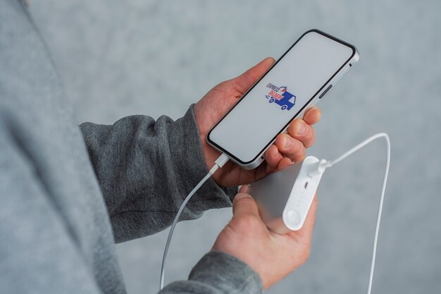 Express-Lieferung in Ihrem Telefon. Ein Mann hält ein Smartphone mit Powerbank und Symbol auf einem weißen Bildschirm in den Händen.