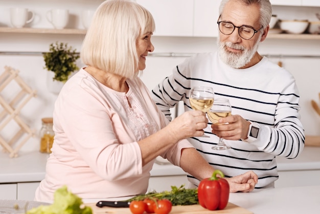 Expressando nossos sentimentos. Sorrindo, alegre casal de idosos em pé na cozinha preparando o jantar, expressando positividade e bebendo champanhe