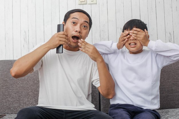 Expressão assustada de pai e filho assistindo televisão vestindo camiseta branca adequada para vestuário