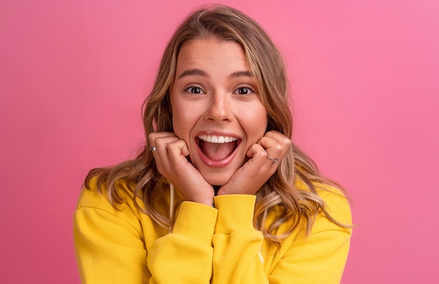 Expressão de rosto fofo de mulher jovem e bonita loira posando com um capuz amarelo na rosa