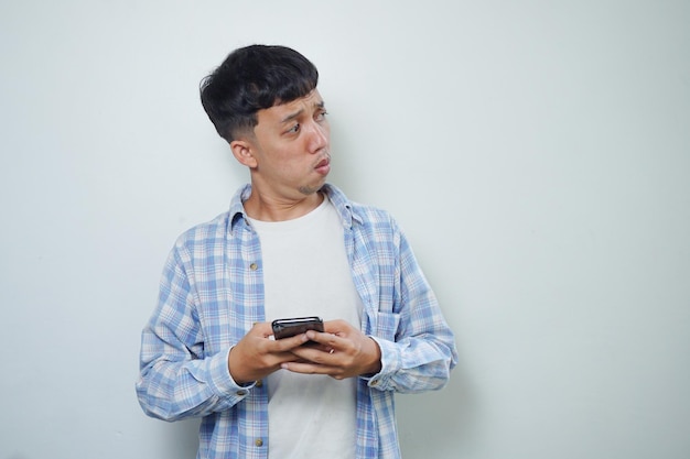 Expressão facial de homem asiático olhando de soslaio enquanto segura o celular isolado no fundo branco