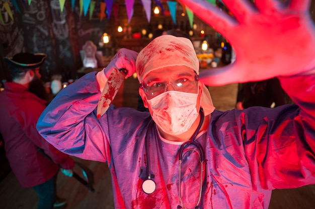 Expressão facial de um homem assustador vestido como um médico segurando uma faca na festa de halloween. Festa de Halloween em uma boate.