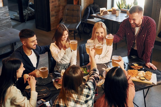 Expressão facial positiva Grupo de jovens amigos sentados juntos no bar com cerveja