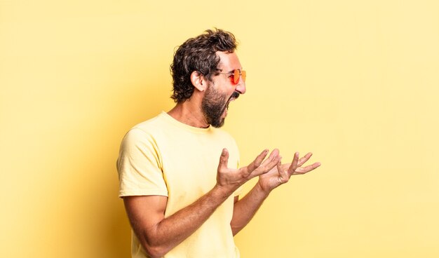 Expressivo homem barbudo louco usando óculos escuros e um espaço de cópia contra a parede amarela