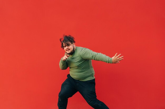 Foto expressivo jovem com excesso de peso em roupas casuais elegantes dançando hip hop no fundo da parede vermelha