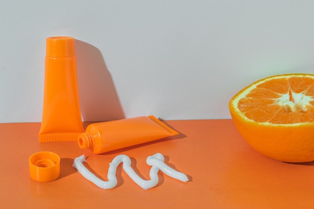 Exprimido de un tubo de crema blanca y media naranja sobre un fondo naranja.