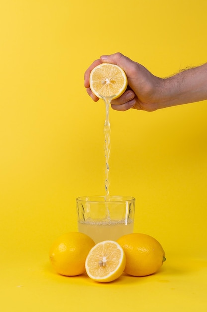 Exprimir jugo de limón en un vaso sobre fondo amarillo