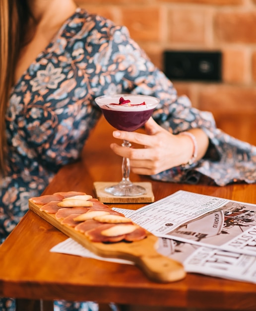 Exquisiter burgunderroter Cocktail in einem speziellen Glas auf einer hölzernen Bartheke vor dem Hintergrund einer Bartheke