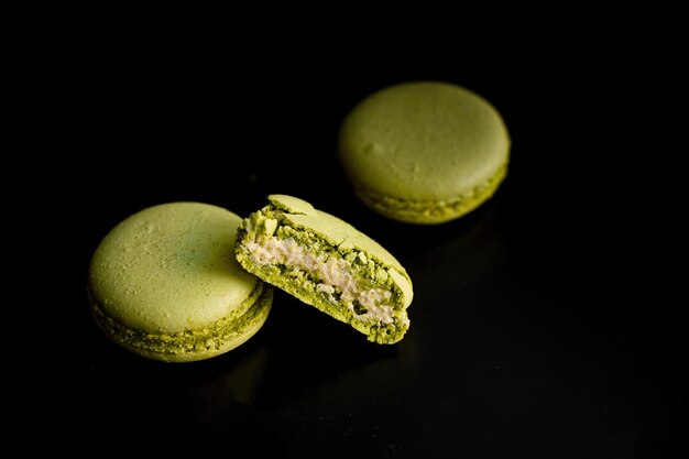 Foto exquisito macarrón de pistacho verde cortado sobre fondo oscuro