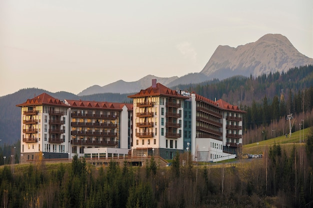 Exterior del complejo pintoresco de gran hotel de lujo, alojamiento turístico con arquitectura moderna en la cresta verde de abeto y cielo despejado. Turismo y recreación.