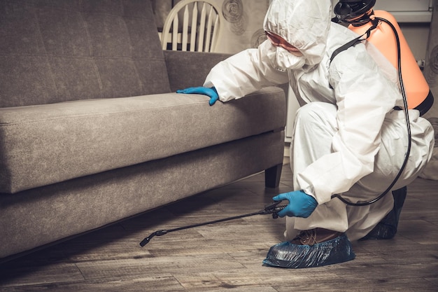 Un exterminador con ropa de trabajo rocía pesticidas con una pistola rociadora. Lucha contra insectos en apartamentos y casas. Desinsectación del local.