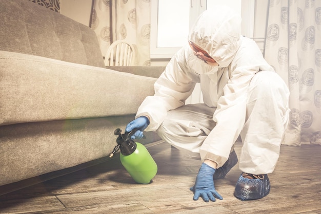 Un exterminador con ropa de trabajo rocía pesticidas con una pistola rociadora. Lucha contra insectos en apartamentos y casas. Desinsectación del local.