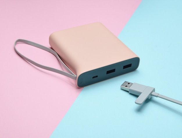 Externer Akku zum Laden von Smartphones und Gadgets mit einer USB-Kabel-Nahaufnahme auf einem rosa-blauen Pastellhintergrund. Power Bank. Moderne Technologien.