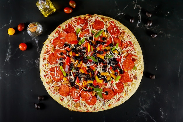 Extra große Pizza mit Oliven und Tomaten auf schwarzem Tisch