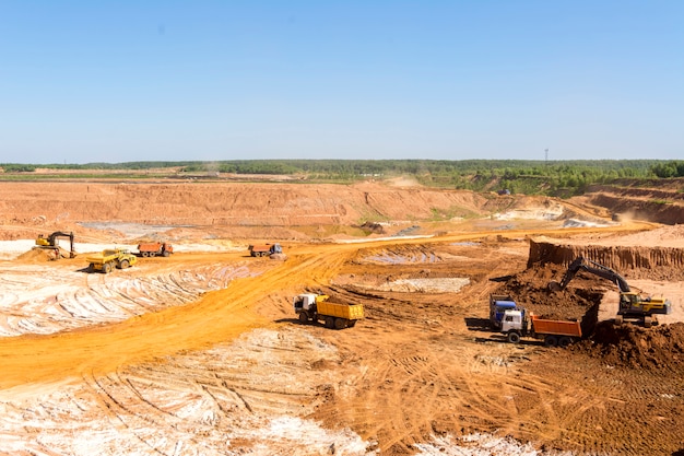 Extração de areia na pedreira. Areia de carregamento de retroescavadeira em caminhões basculantes.