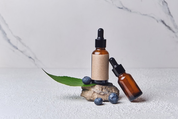 Extracto cosmético de arándanos para el cuidado de la piel para spa, vitaminas para la salud, efecto fresco, tubo blanco con crema ecológica natural para la piel del rostro. Cosmética ecológica. Ingredientes de arándanos, botella marrón sobre soporte de piedra