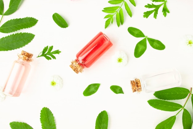 Extracto de flor de rosa en botellas de vidrio sobre una mesa de madera blanca con hojas de plantas