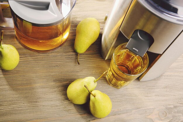 Extractor de jugo de acero inoxidable con peras y vaso de jugo sobre fondo de madera de cerca