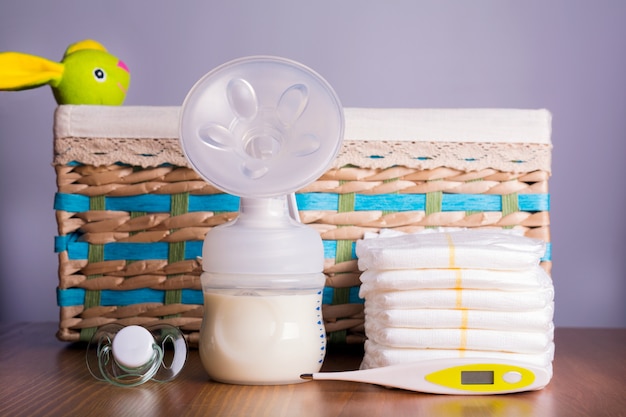 Extractor de leche, termómetros, pañales y un pezón de bebé con cesta de mimbre con un juguete.